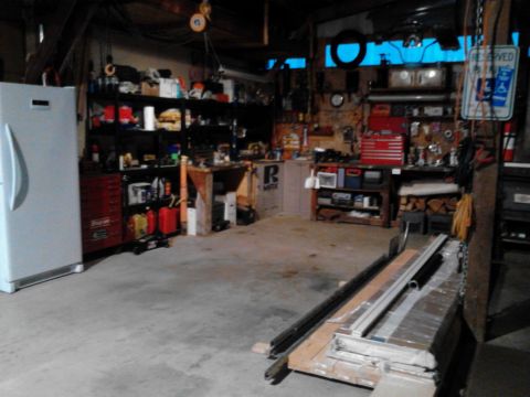 1989 Ford Bronco - This is a cluttered garage scene with shelves full of items, a refrigerator, toolboxes, and lumber stacked on the floor. A workbench is vis…