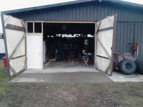 1989 Ford Bronco - A wide open garage door reveals the interior of a workshop. Two large, rustic doors are open, one to the left and one to the right, with a…