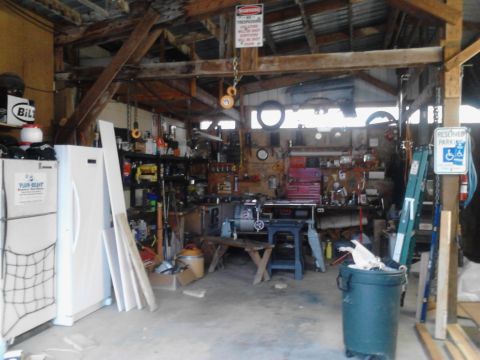 1989 Ford Bronco - This is a cluttered garage workshop with various tools, equipment, and storage shelves. A white refrigerator is visible on the left side of…