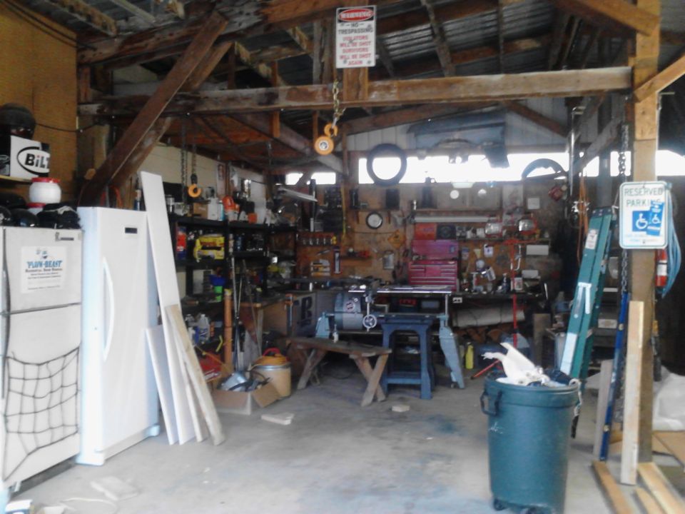 Cluttered garage workshop with tools, shelves, and a refrigerator.