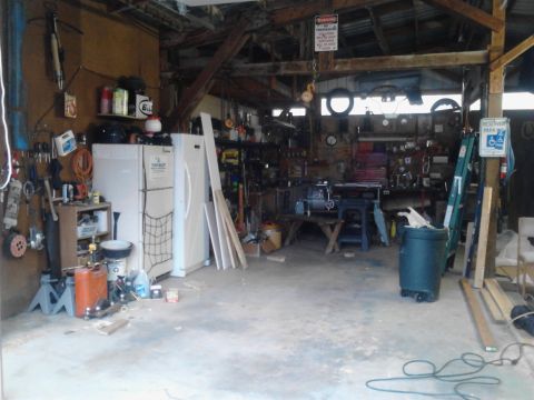 1989 Ford Bronco - This is a cluttered garage scene with various tools, appliances, and building materials. A workbench with a vise and a blue stand are visib…