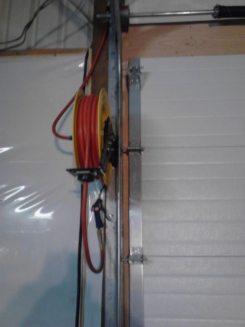1989 Ford Bronco - A red air hose is wound on a yellow reel mounted on a metal bracket next to a garage door.