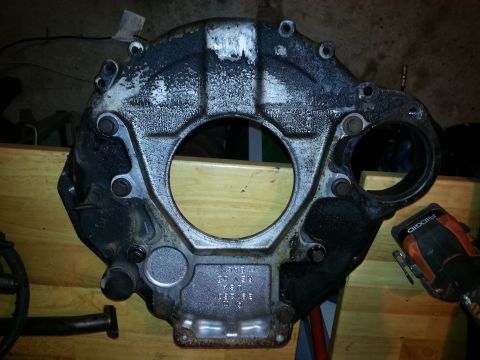 1994 Ford Bronco - A black and silver transmission bell housing is shown mounted on a wooden surface. The part has several bolts and a large central opening,…