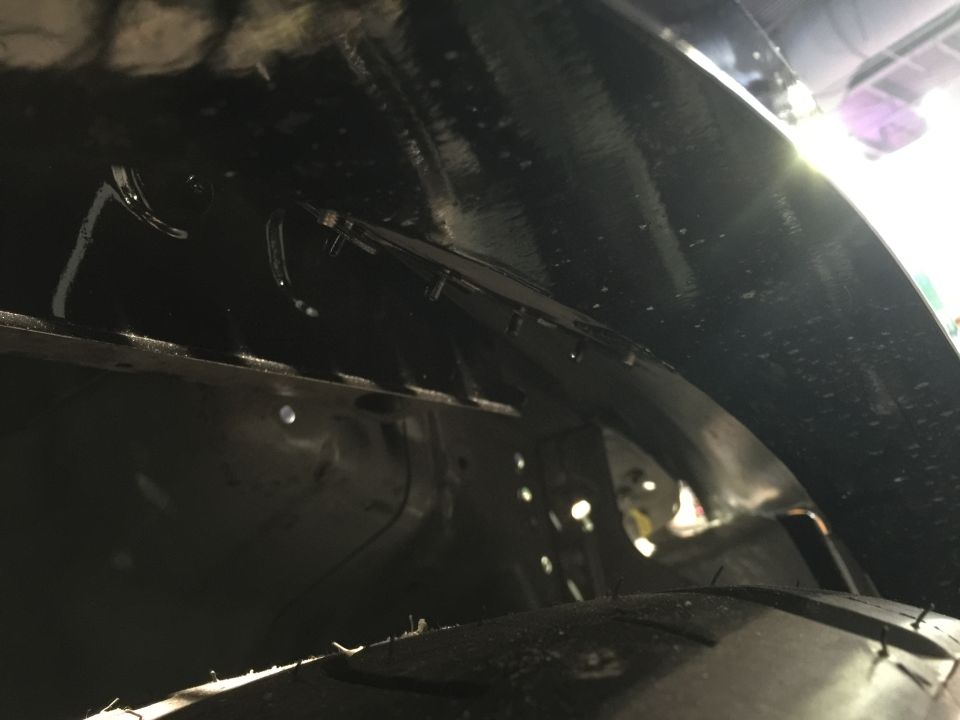 Underside of a black wheel well showing tire and inner fender structure with mounting points.