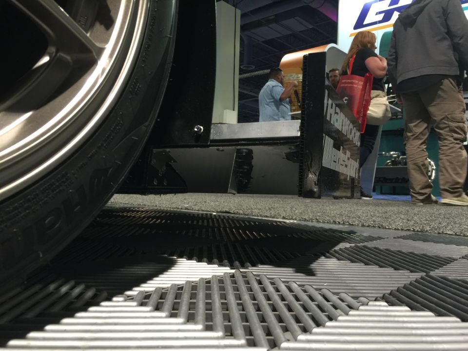 Close-up of a vehicle's wheel and fender at an auto show, with people in the background