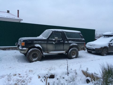 1987 Ford Bronco - A 1987 Ford Bronco sits covered in snow, with another vehicle nearby.