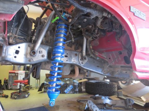 1996 Ford Bronco - The front suspension of a red Ford Bronco is shown with a new blue coilover shock being installed.