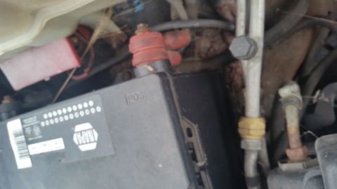 1991 Ford LTD Crown Victoria - Photograph of a car battery and positive terminal boot in an engine compartment, not a technical document.
