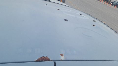 1991 Ford LTD Crown Victoria - Photograph of a gray car hood with rust spots and holes, not a technical document.