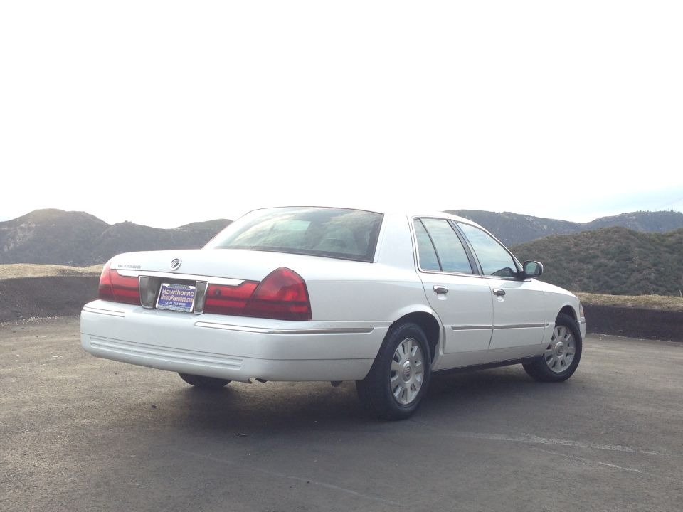 White sedan parked on a road with hills in the background.