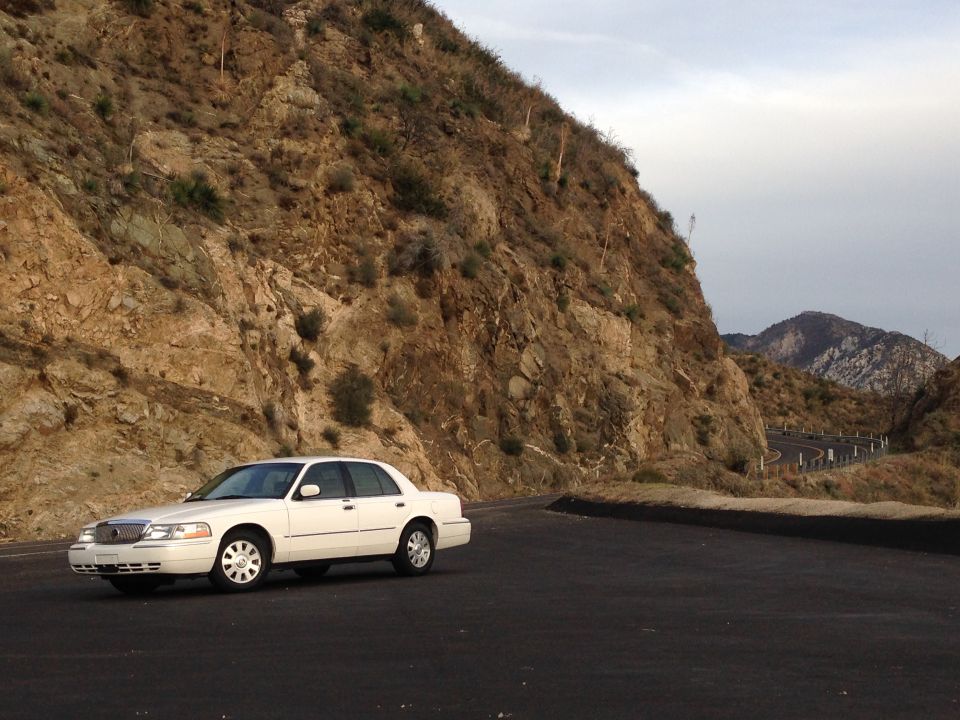 White sedan parked on a winding mountain road.