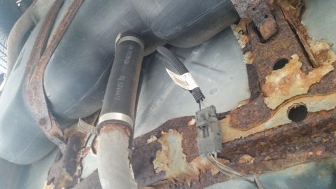 1991 Ford LTD Crown Victoria - Photograph of a corroded undercarriage frame with connector and hose, not a technical document.