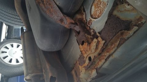 1991 Ford LTD Crown Victoria - Photograph of a severely rusted floor pan and frame over the exhaust, not a technical document.