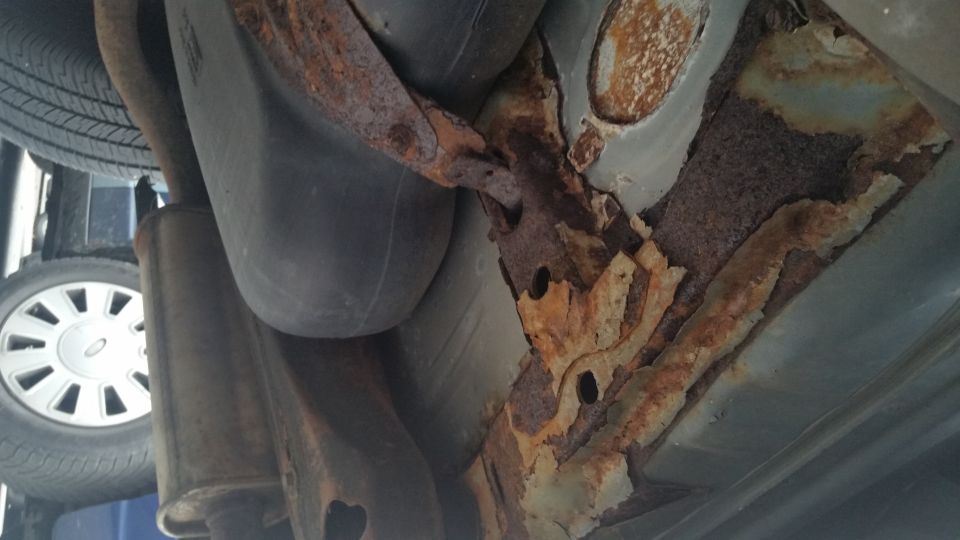 Severely rusted floor pan and frame above an exhaust pipe