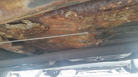1991 Ford LTD Crown Victoria - Photograph of a rusted underbody frame rail and floor, not a technical document.
