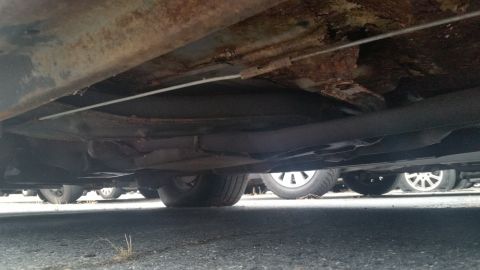 1991 Ford LTD Crown Victoria - Photograph of a rust-perforated underbody panel from beneath the car, not a technical document.