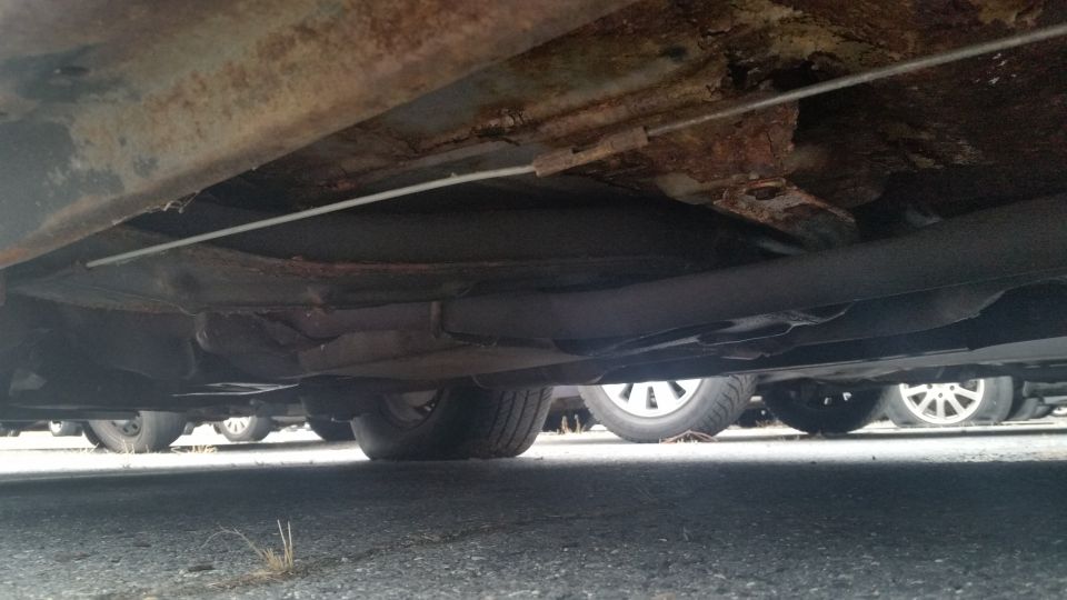 Rust-perforated underbody panel viewed from beneath the car