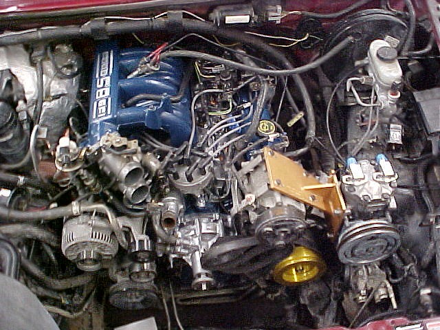 Engine bay of a vehicle showing blue 5.8 EFI intake, alternator, AC compressor and brake booster