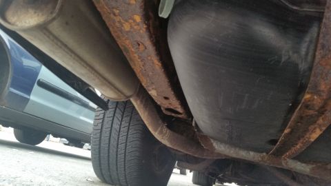 1991 Ford LTD Crown Victoria - Photograph of a vehicle underbody with surface rust on the frame, exhaust pipe and fuel tank, not a technical document.