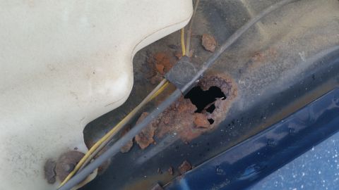 1991 Ford LTD Crown Victoria - Photograph of a rusted-through vehicle body seam with exposed wires, not a technical document.
