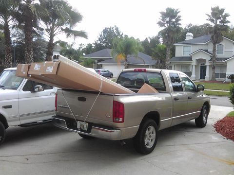 1994 Ford Bronco - A gold Dodge Ram pickup truck is parked next to a white Ford Bronco, with large cardboard boxes loaded in the bed of the Dodge. The boxes e…
