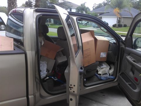 1994 Ford Bronco - The interior of a gold pickup truck is filled with cardboard boxes and other items. The driver's side door is open, revealing the contents…