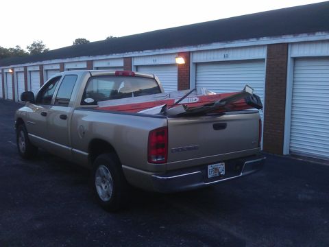 1994 Ford Bronco - A gold Dodge pickup truck is parked in front of a row of storage units. The truck bed contains several long items, possibly construction ma…