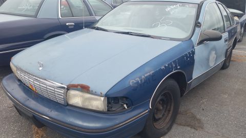 1991 Ford LTD Crown Victoria - Photograph of the front of a blue Chevrolet sedan in a salvage lot, not a technical document.