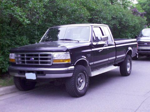 1997 Ford F-250 - A black 1997 Ford F-250 pickup truck is parked on a street next to another vehicle.