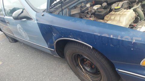 1991 Ford LTD Crown Victoria - Photograph of a faded blue ex-police sedan's front fender and wheel, not a document.