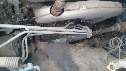 1991 Ford LTD Crown Victoria - Photograph of a corroded exhaust manifold and routing hoses under the hood, not a document.