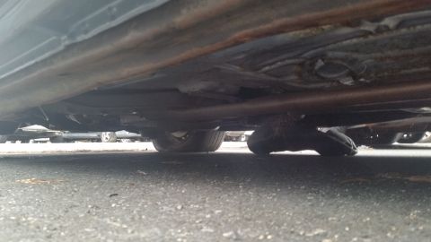 1991 Ford LTD Crown Victoria - Low-angle photograph beneath a vehicle rocker panel showing exhaust, not a document.