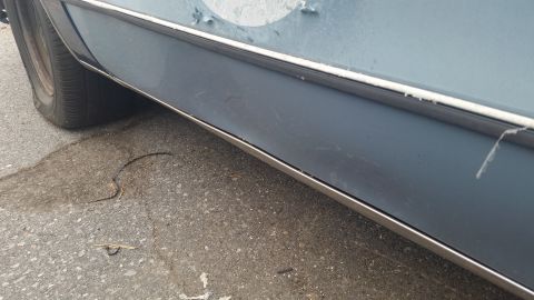 1991 Ford LTD Crown Victoria - Photograph of a blue sedan's lower rocker panel and chrome trim, not a document.
