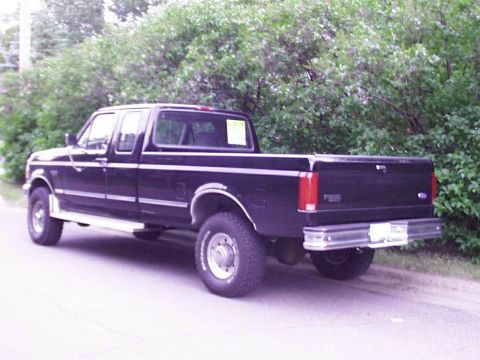 1997 Ford F-250 - This black 1997 Ford F-250 pickup truck is viewed from a three-quarter front angle, parked beside a tree line.