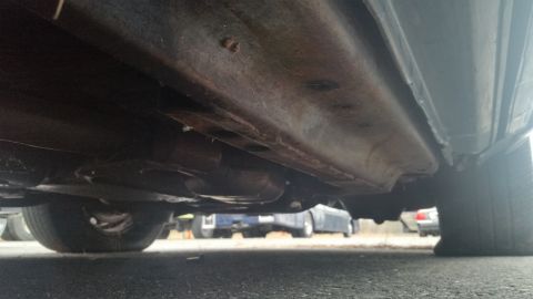 1991 Ford LTD Crown Victoria - Low-angle photograph of a car's rusty underbody, floor pan and exhaust, not a document.