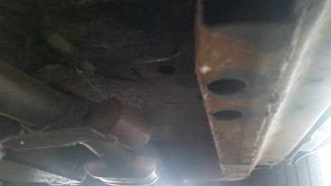 1991 Ford LTD Crown Victoria - Close-up photograph of a vehicle's underbody frame rail and exhaust, not a document.