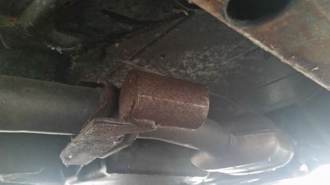 1991 Ford LTD Crown Victoria - Close-up photograph of a rusty exhaust muffler and pipes under a vehicle, not a document.