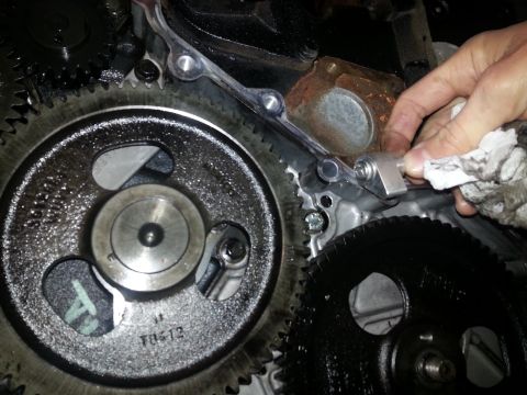 1994 Ford Bronco - A close-up view of engine gears, with a hand holding a rag wiping a metal component near the gears. The gears appear to be part of an inter…