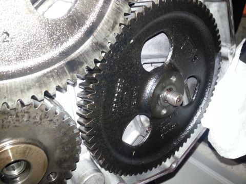 1994 Ford Bronco - A close-up view of two meshed gears, one black and one silver, both covered in oil. The black gear has a bolt protruding from its center hu…