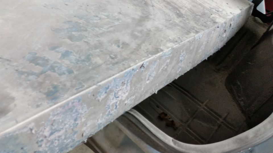 Bare metal panel edge with sanded primer spots on a work stand