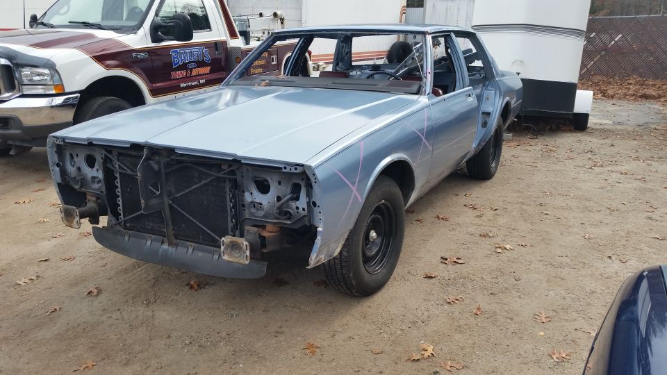 Light blue sedan project car with front clip removed in a yard
