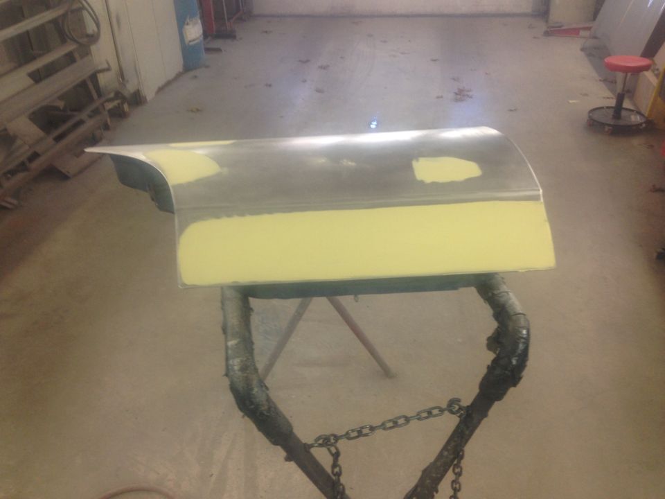 Yellow-bodyfiller fender panel on a work stand in a shop