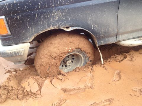 1987 Ford Bronco - The front driver's side wheel of a black Ford Bronco is deeply stuck in thick, wet mud. The vehicle is covered in mud splatters, indicating…