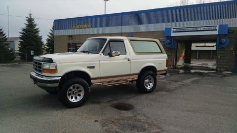 1994 Ford Bronco - A white 1994 Ford Bronco is parked in front of a laundromat and a car wash. The vehicle is shown from a 3/4 front angle, highlighting its t…