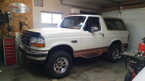 1994 Ford Bronco - A white 1990s Ford Bronco with brown lower body trim is parked in a garage next to a red toolbox and a snowblower.