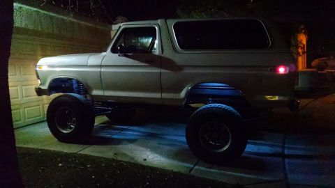 1979 Ford Bronco - A lifted, white 1979 Ford Bronco is parked in a driveway at night, illuminated by undercarriage lights. The vehicle is positioned in front…