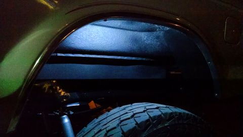 1979 Ford Bronco - The underside of a vehicle's wheel well is illuminated by blue light, showing the tire and part of the vehicle's frame.