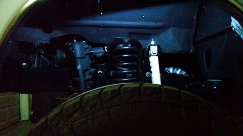 1979 Ford Bronco - The underside of a vehicle's suspension system is visible, featuring a black coil spring, a white shock absorber, and part of a tire.