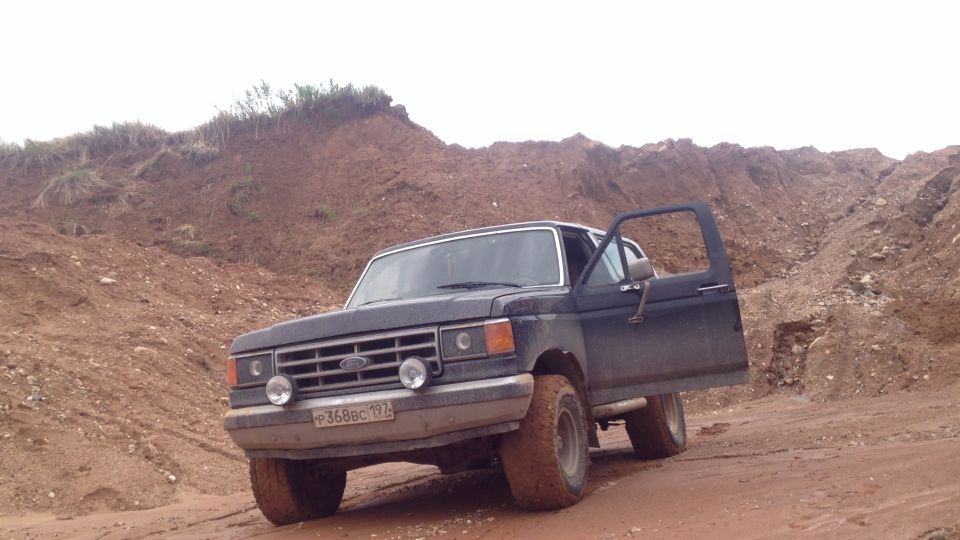 Dark Ford Bronco with open door on muddy road in sandy hills