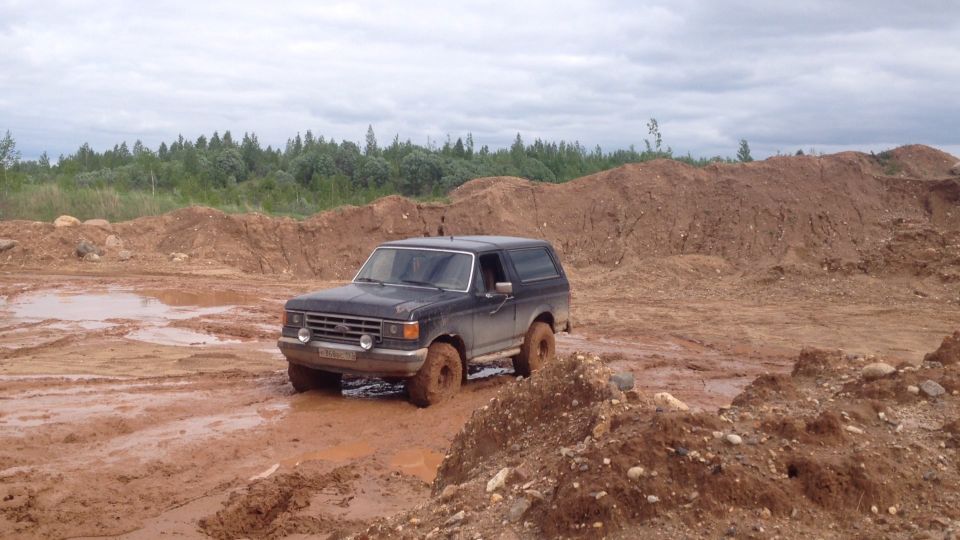 1987 Ford Bronco driving through mud and dirt piles.